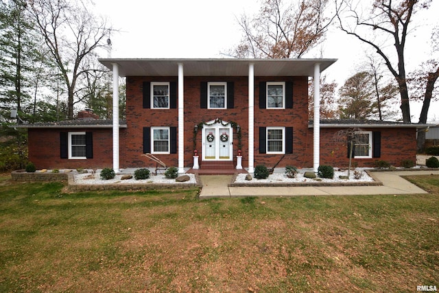 neoclassical / greek revival house with a chimney, a front lawn, and brick siding