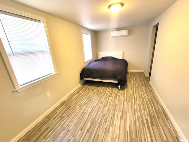 bedroom with baseboards, a wall unit AC, and wood finished floors