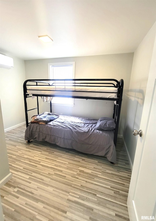 bedroom featuring an AC wall unit, baseboards, and wood finished floors