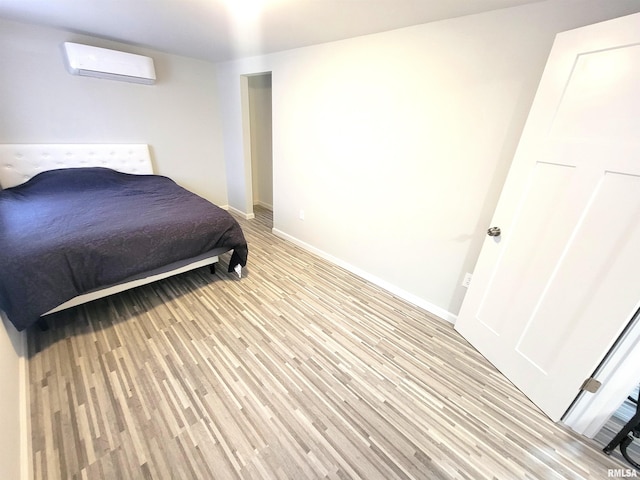 bedroom featuring a wall mounted air conditioner, light wood finished floors, and baseboards