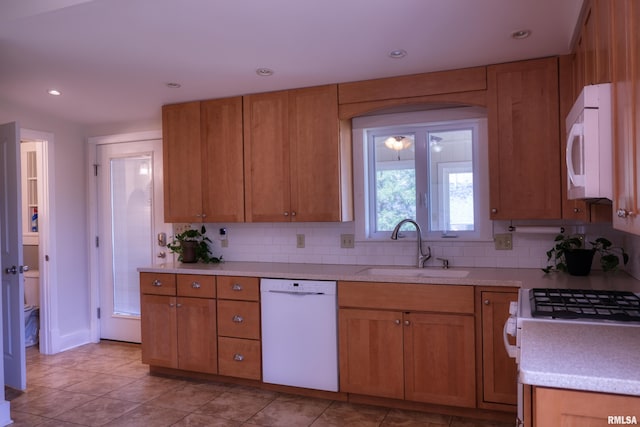 kitchen with white appliances, light countertops, backsplash, brown cabinetry, and a sink