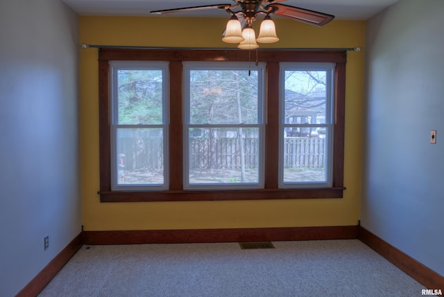 carpeted spare room featuring a wealth of natural light, visible vents, baseboards, and ceiling fan