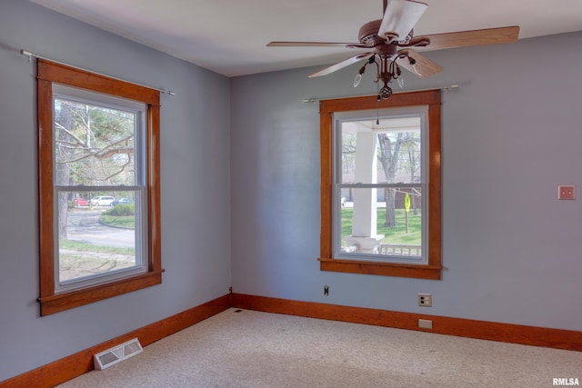 carpeted spare room with ceiling fan, baseboards, visible vents, and a wealth of natural light