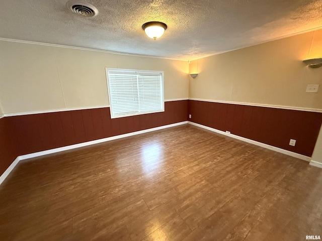 empty room featuring crown molding, a textured ceiling, visible vents, wood finished floors, and wainscoting