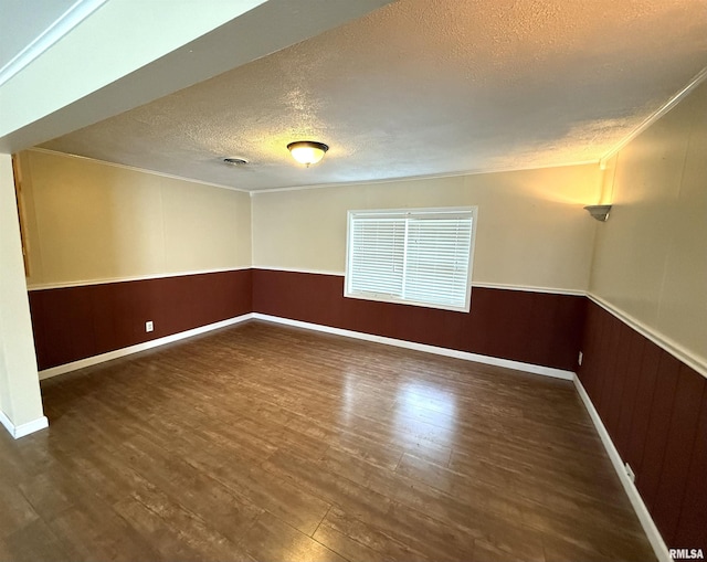 unfurnished room with a textured ceiling, wood finished floors, crown molding, and a wainscoted wall