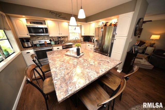 kitchen with dark wood-style flooring, light stone counters, backsplash, a kitchen bar, and appliances with stainless steel finishes