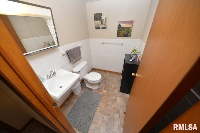 bathroom featuring toilet, a sink, wainscoting, and tile walls