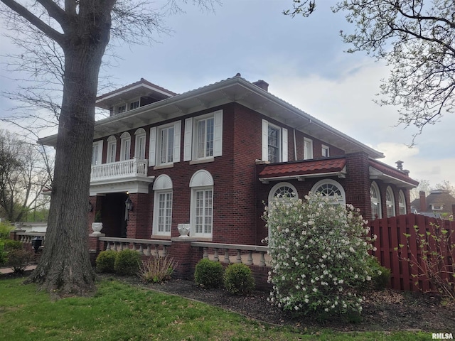 view of side of property with a balcony, fence, and brick siding