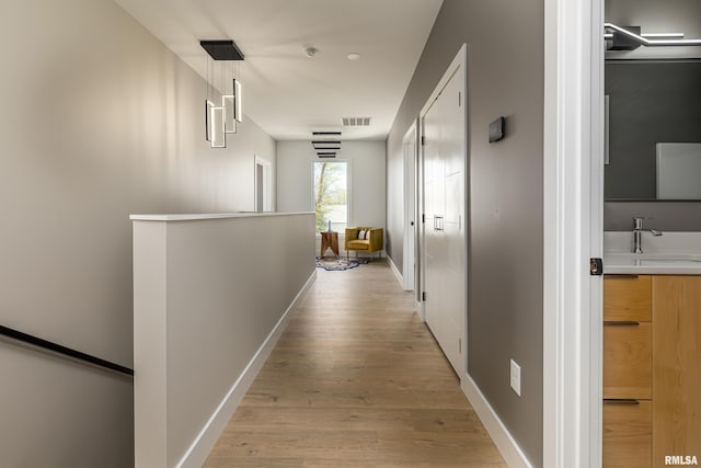 corridor featuring visible vents, a sink, an upstairs landing, light wood finished floors, and baseboards