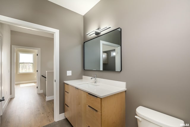 half bath featuring toilet, wood finished floors, vanity, and baseboards