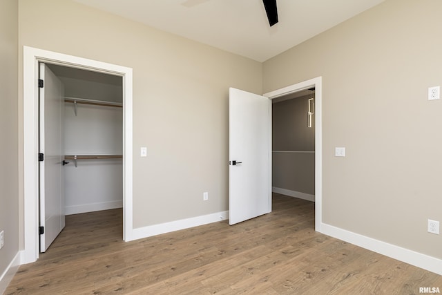 unfurnished bedroom with a walk in closet, light wood-style floors, a closet, and baseboards