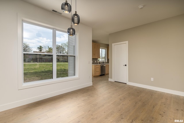 unfurnished living room with light wood-type flooring, a sink, baseboards, and visible vents