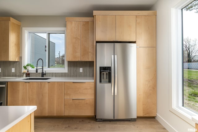 kitchen featuring light wood-style flooring, light brown cabinetry, appliances with stainless steel finishes, light countertops, and a sink