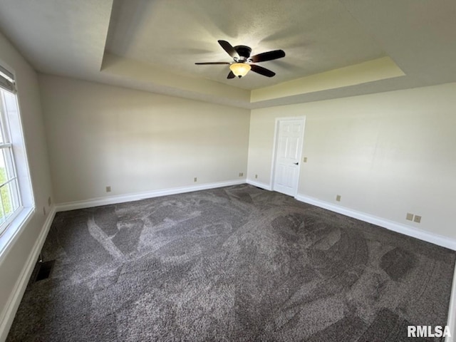 unfurnished room with visible vents, baseboards, dark carpet, a ceiling fan, and a tray ceiling