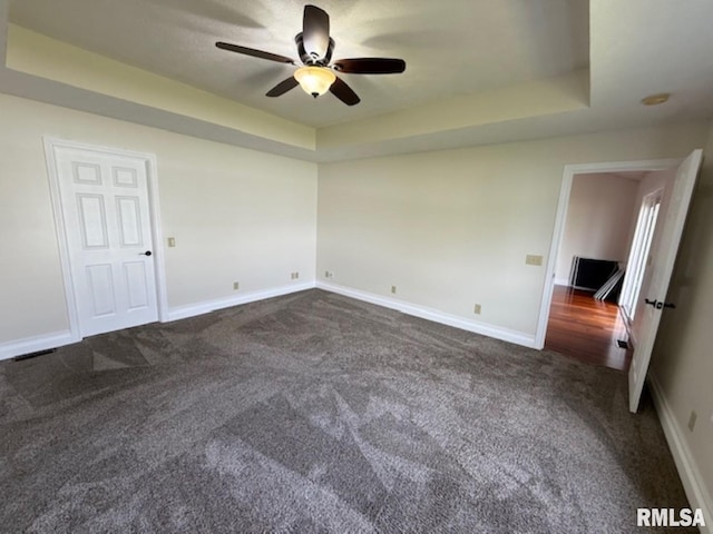 empty room featuring dark carpet, a raised ceiling, ceiling fan, and baseboards