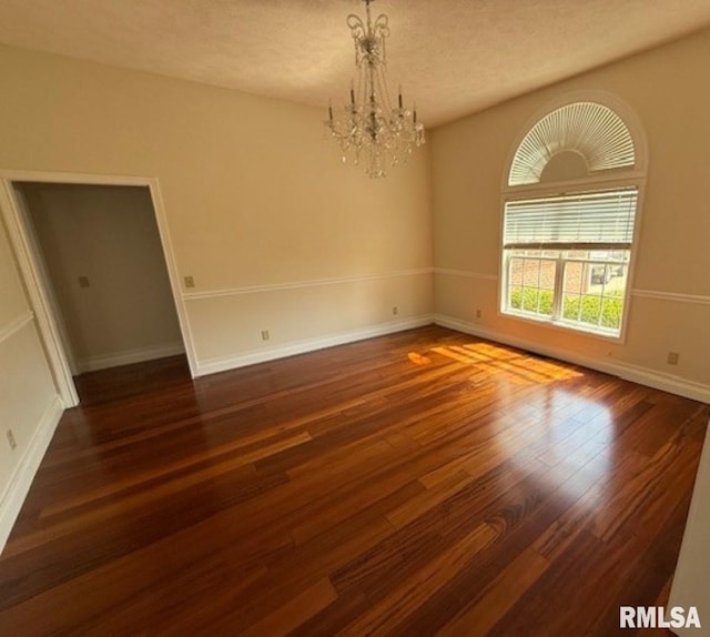 empty room with wood finished floors, a notable chandelier, and baseboards