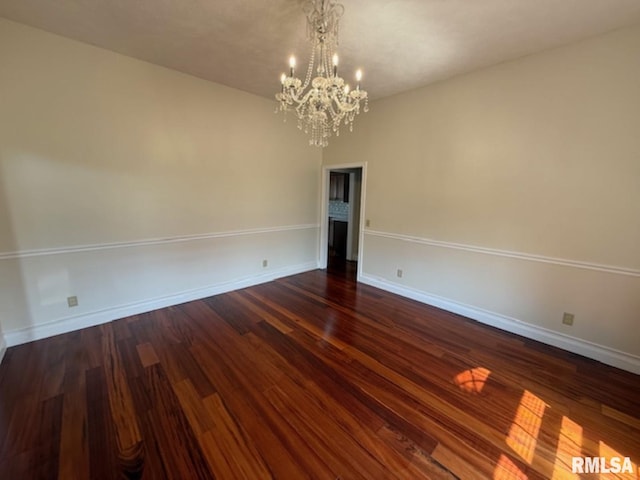 empty room featuring dark wood-type flooring, baseboards, and a chandelier