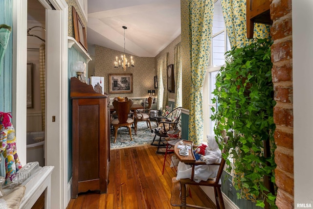 hall featuring wallpapered walls, wood-type flooring, vaulted ceiling, and an inviting chandelier