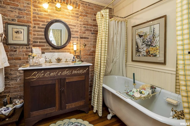 bathroom featuring a freestanding tub, vanity, brick wall, wainscoting, and wood finished floors