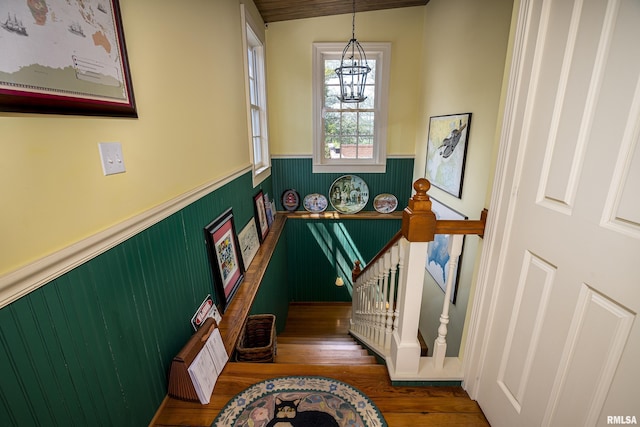 stairs featuring wood finished floors, a notable chandelier, and a wainscoted wall