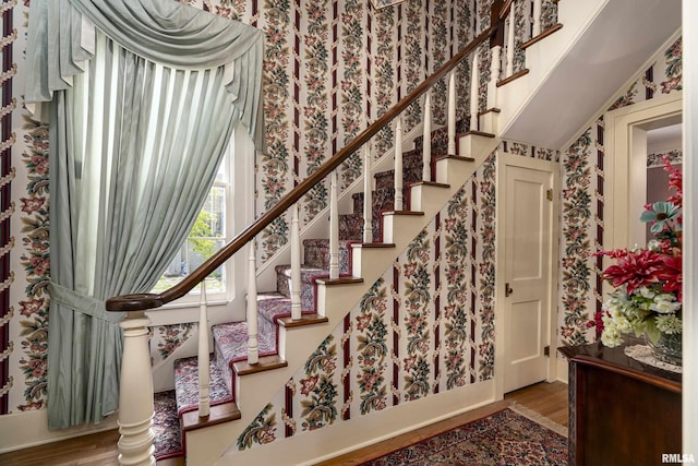 staircase with wallpapered walls and wood finished floors