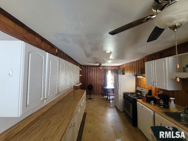 kitchen featuring white appliances, wooden walls, a ceiling fan, white cabinets, and a sink