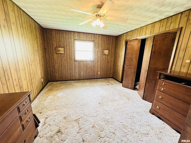 unfurnished bedroom featuring ceiling fan, carpet floors, wood walls, and a closet
