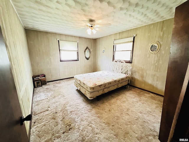 carpeted bedroom featuring ceiling fan and wood walls