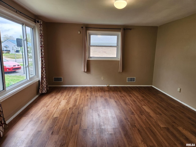 unfurnished room with dark wood finished floors, visible vents, and baseboards