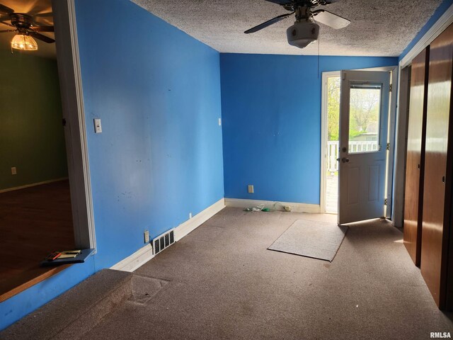 carpeted empty room with a textured ceiling, baseboards, ceiling fan, and visible vents