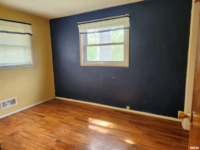 unfurnished room with hardwood / wood-style floors, visible vents, and baseboards