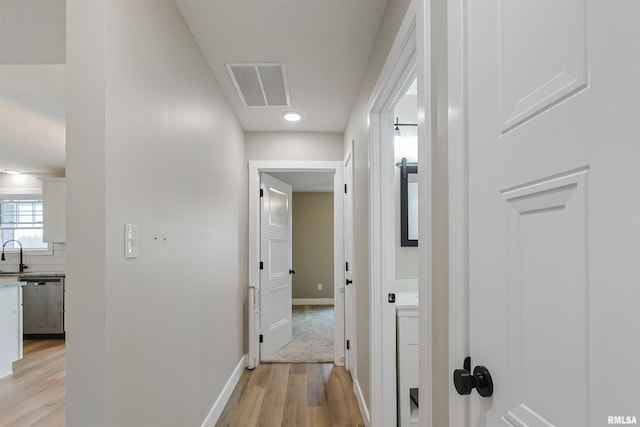 hallway with baseboards, light wood-style floors, visible vents, and a sink