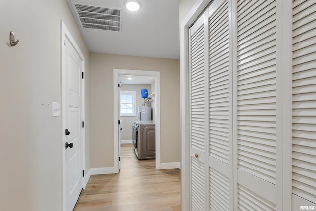 hall with electric water heater, washer / dryer, light wood-style flooring, baseboards, and visible vents