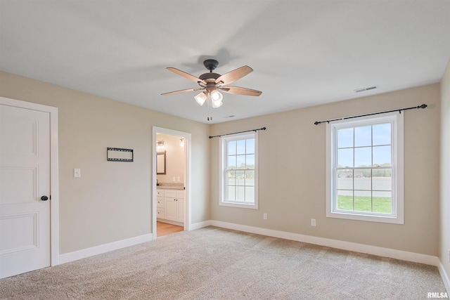 unfurnished bedroom with visible vents, a ceiling fan, connected bathroom, baseboards, and light colored carpet