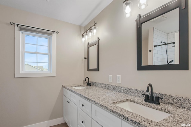 full bathroom with a tile shower, double vanity, baseboards, and a sink