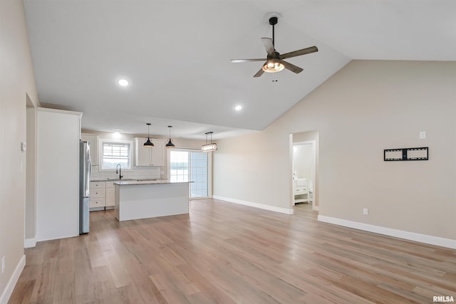unfurnished living room featuring light wood-style flooring, baseboards, ceiling fan, and a sink