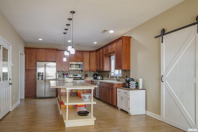 kitchen with a barn door, light wood-style floors, stainless steel appliances, backsplash, and pendant lighting
