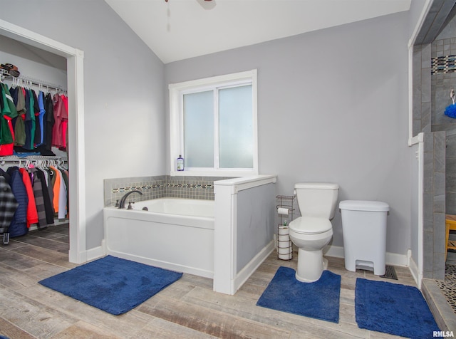 bathroom featuring wood finished floors, toilet, tiled shower, a bath, and vaulted ceiling