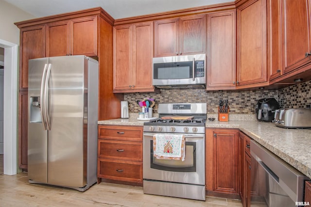kitchen featuring light wood-style floors, decorative backsplash, brown cabinetry, and stainless steel appliances