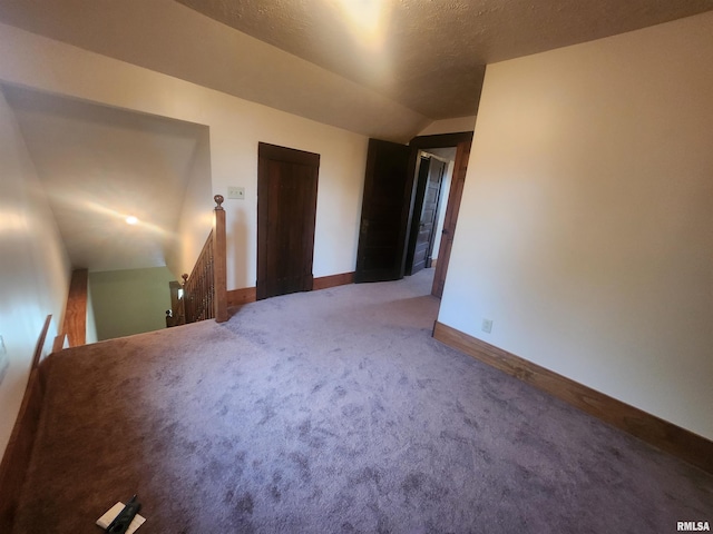 unfurnished room with vaulted ceiling, a textured ceiling, carpet flooring, and baseboards