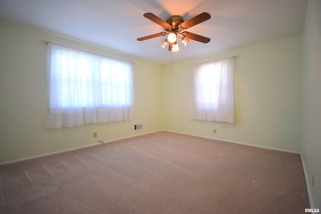 carpeted spare room featuring baseboards, visible vents, a ceiling fan, and a wealth of natural light