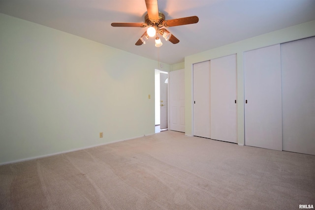 unfurnished bedroom with multiple closets, a ceiling fan, and light carpet