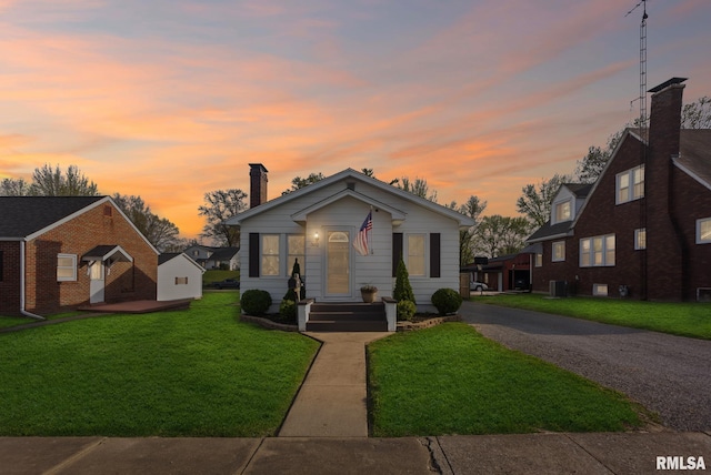 bungalow-style home with gravel driveway, a front lawn, a chimney, and cooling unit