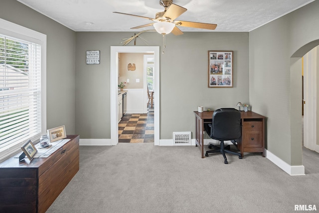 carpeted office space featuring arched walkways, visible vents, baseboards, and ceiling fan
