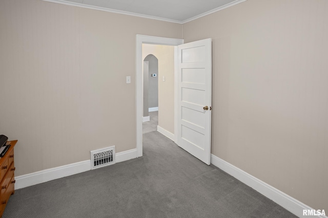 spare room featuring dark colored carpet, visible vents, ornamental molding, arched walkways, and baseboards