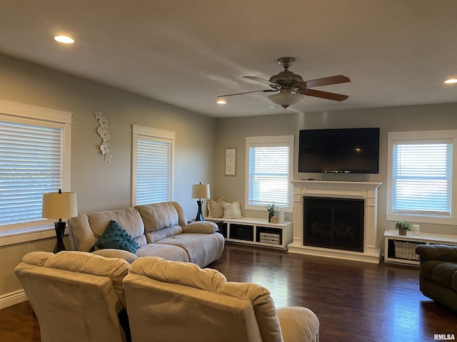 living area with ceiling fan, dark wood-type flooring, a fireplace with raised hearth, and recessed lighting