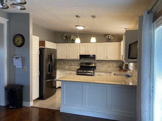 kitchen with stainless steel range with gas cooktop, a peninsula, a sink, black fridge, and under cabinet range hood