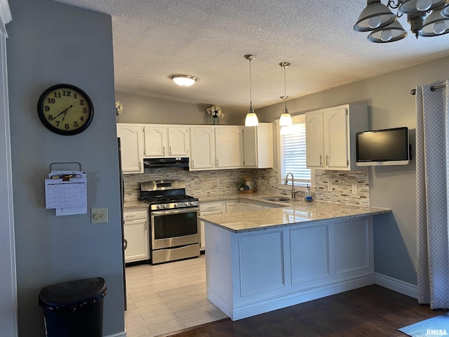 kitchen featuring tasteful backsplash, a sink, stainless steel gas stove, a peninsula, and under cabinet range hood