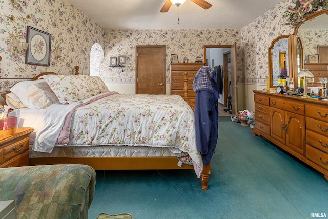 carpeted bedroom with wallpapered walls, a wainscoted wall, a textured ceiling, and ceiling fan