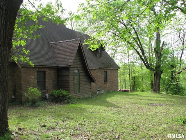 view of side of property featuring a lawn, a shingled roof, and brick siding